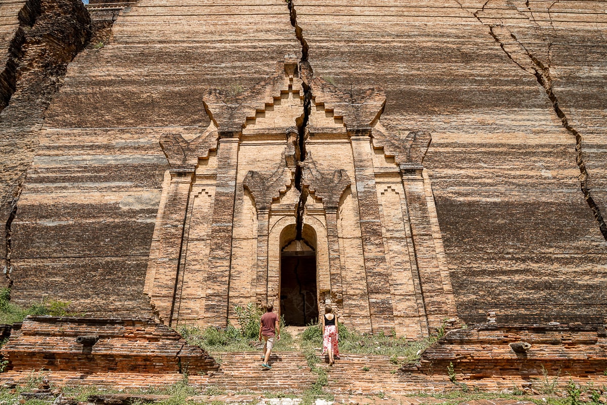 An enormous brick building that looks like a cliff with a huge doorway and a couple walking towards it