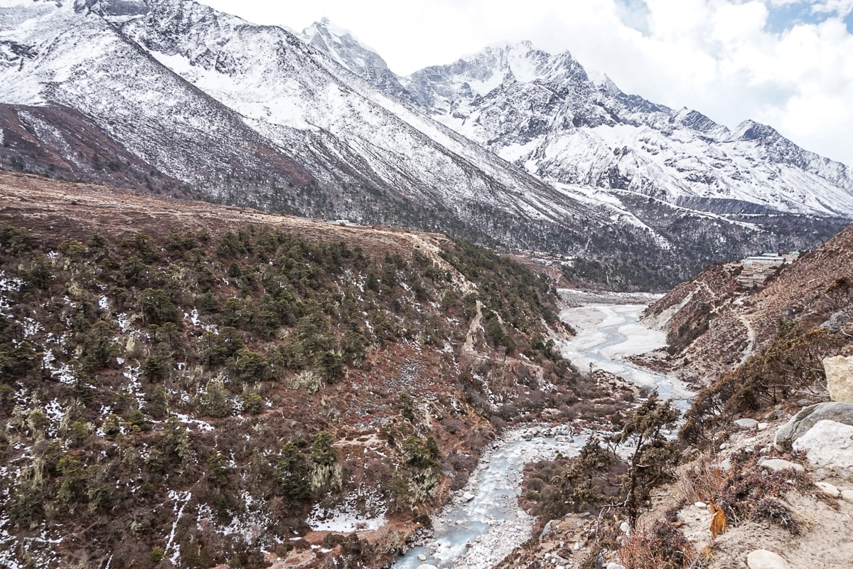 A turquoise river in a valley with snow covered mountains in the background