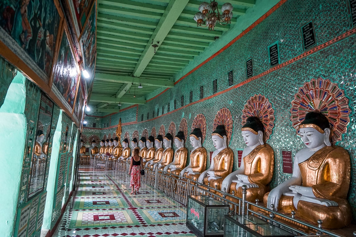 A row of dozens of buddha statues sitting inside a green interior of a pagoda