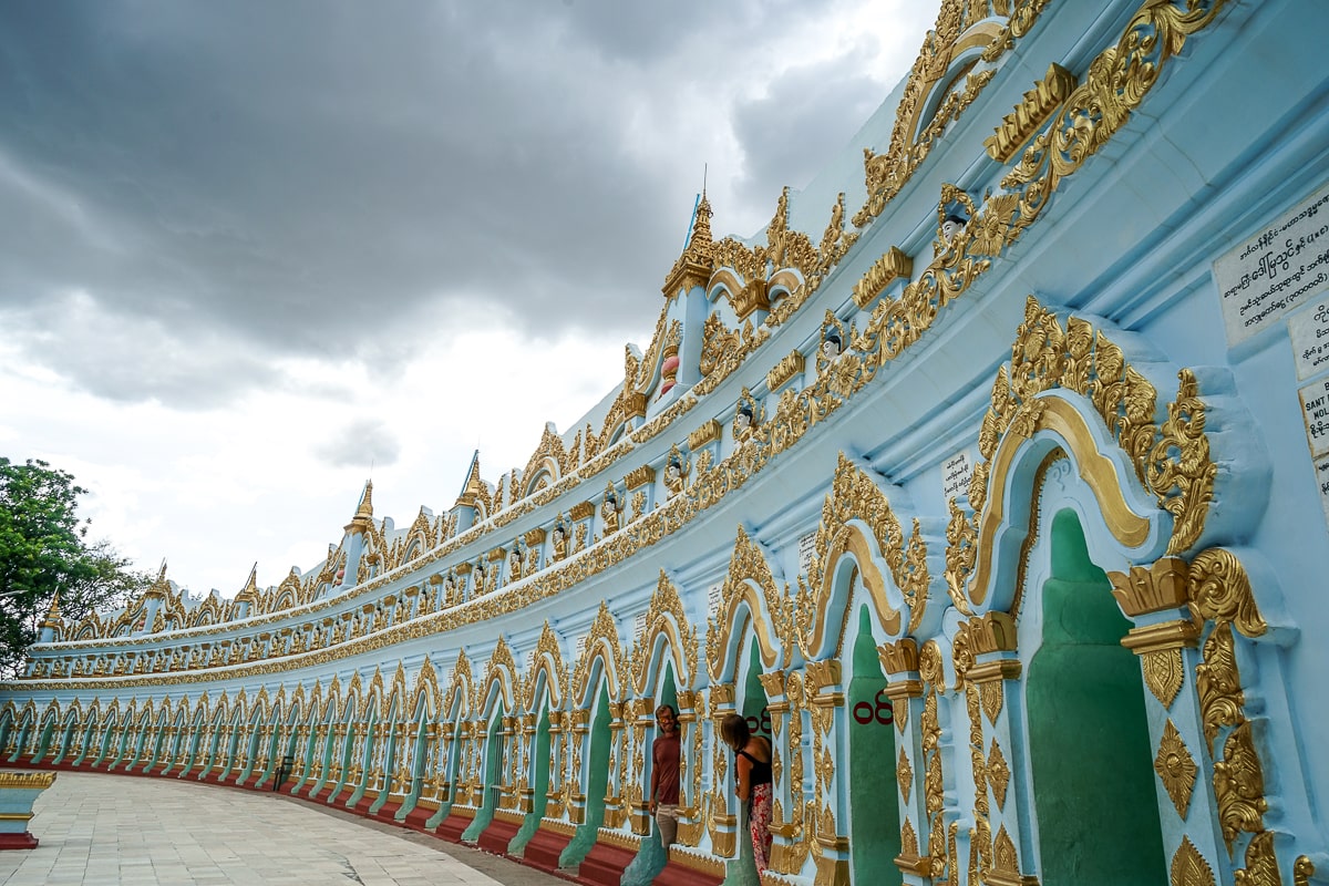 A sky blue and gold pagoda with dozens of small doorways, a couple standing in two of them