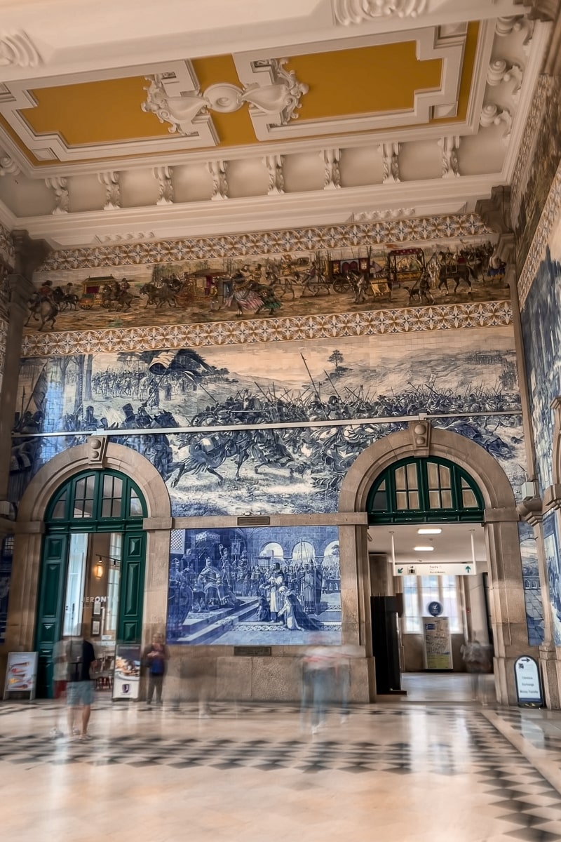 Inside an ornately decorated train station with blue and white azulejo tiles and a yellow ceiling