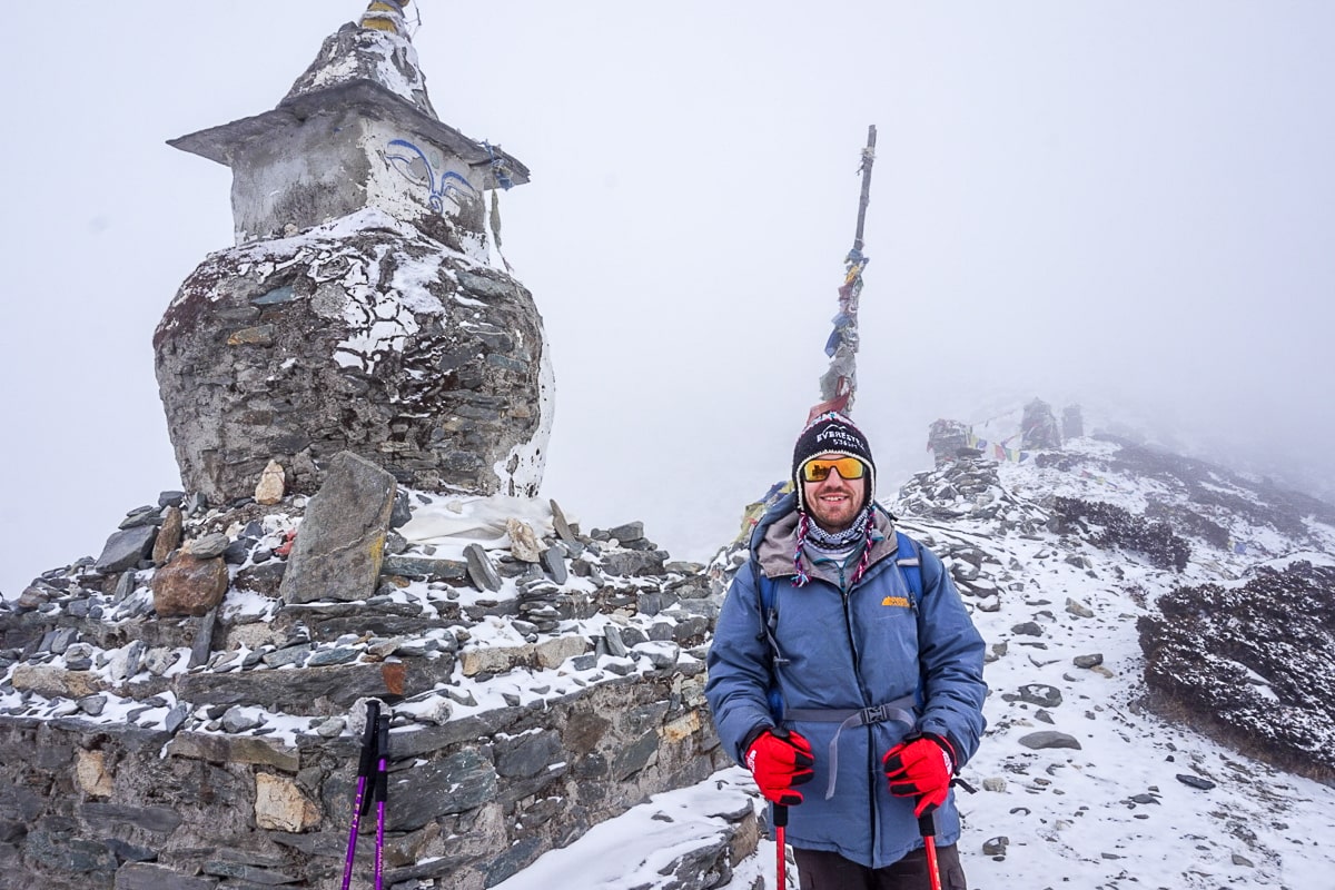 A man in a blue winter jacket standing next to a stone stupa in a snowy, foggy landscape