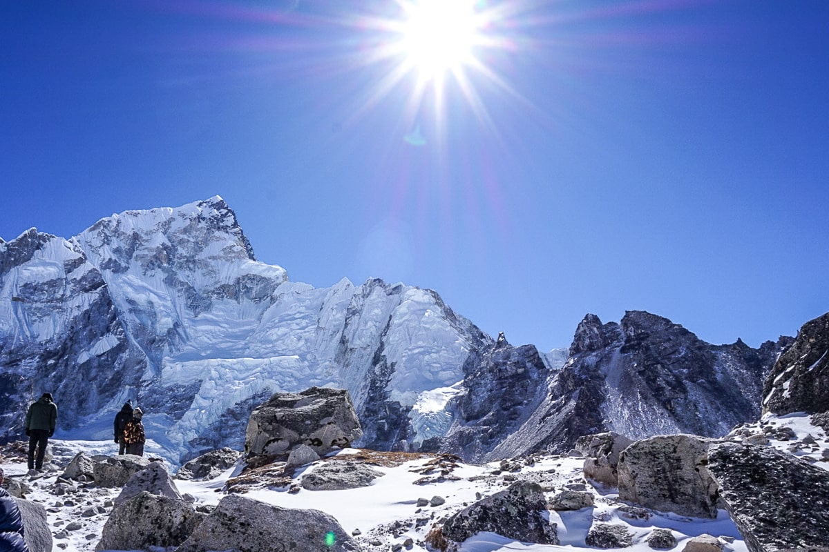 The sun shining brightly in a blue cloudless sky above huge, snow-capped mountains