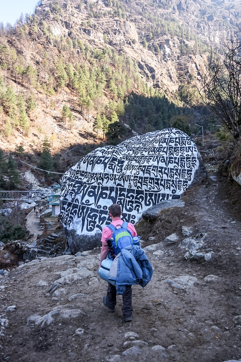 A man walking in front of a rock with Tibetan carvings painted white and black