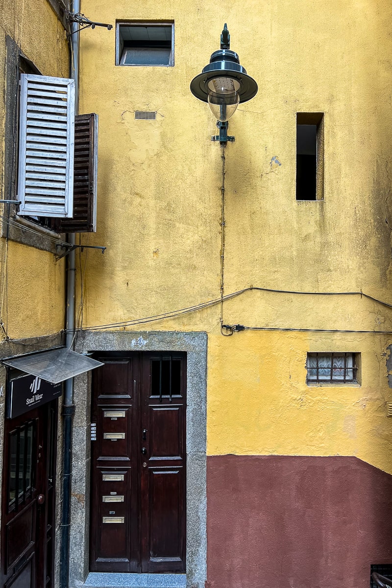 A pastel yellow wall with quirky elements like door, wooden slat windows and an ornate street lamp