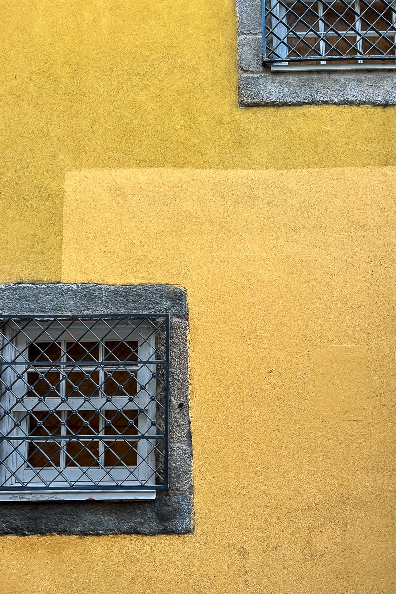 A yellow pastel wall with windows with metal grate coverings