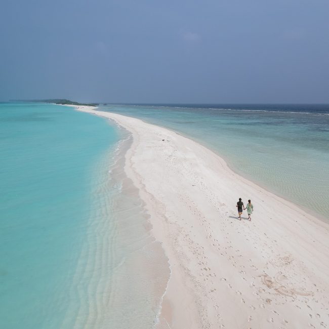 A couple walk along the bright white sandbank at the southern end of Dhigurah