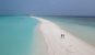 A couple walk along the bright white sandbank at the southern end of Dhigurah