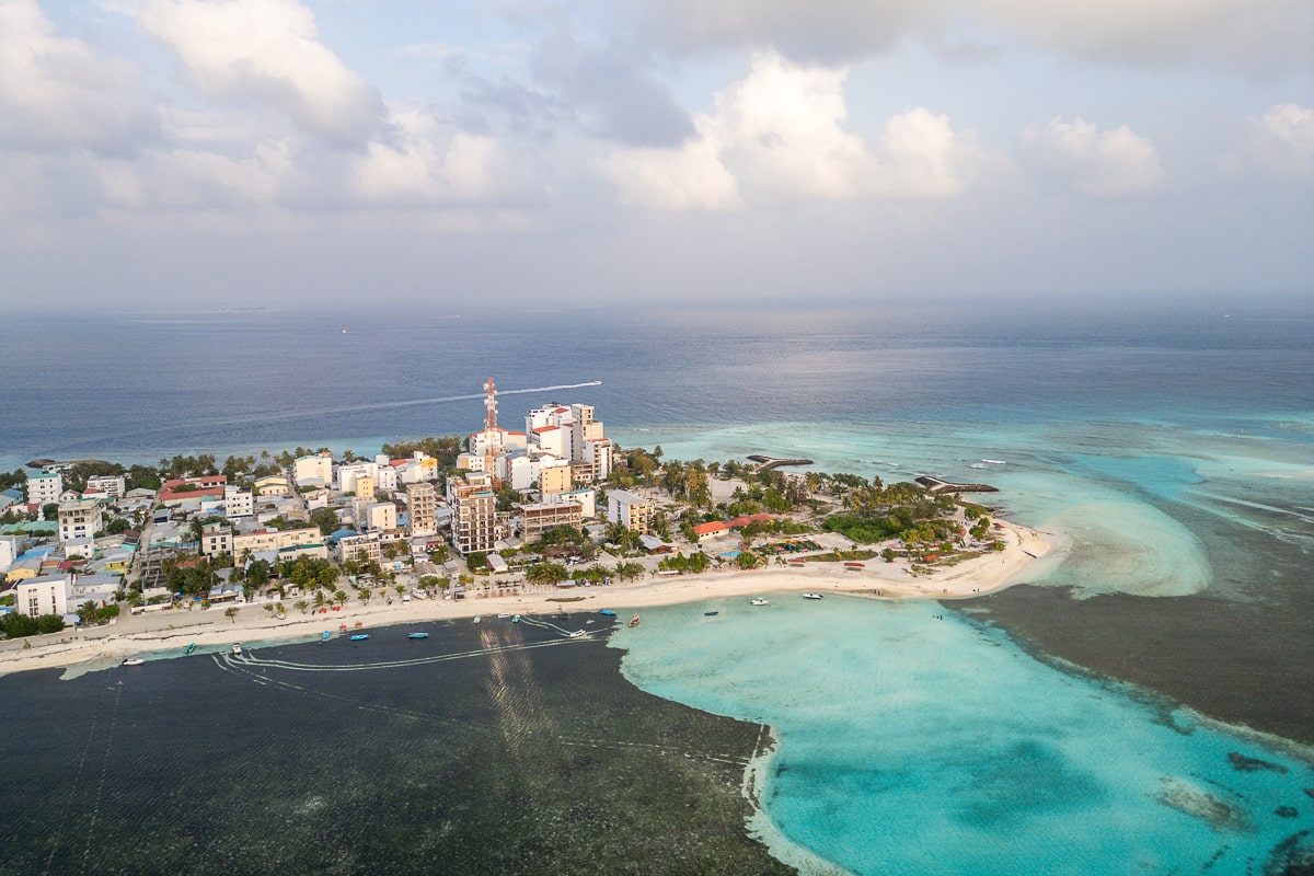 An aerial shot of Maafushi Island surrounded by clear waters with sea grass and coral areas