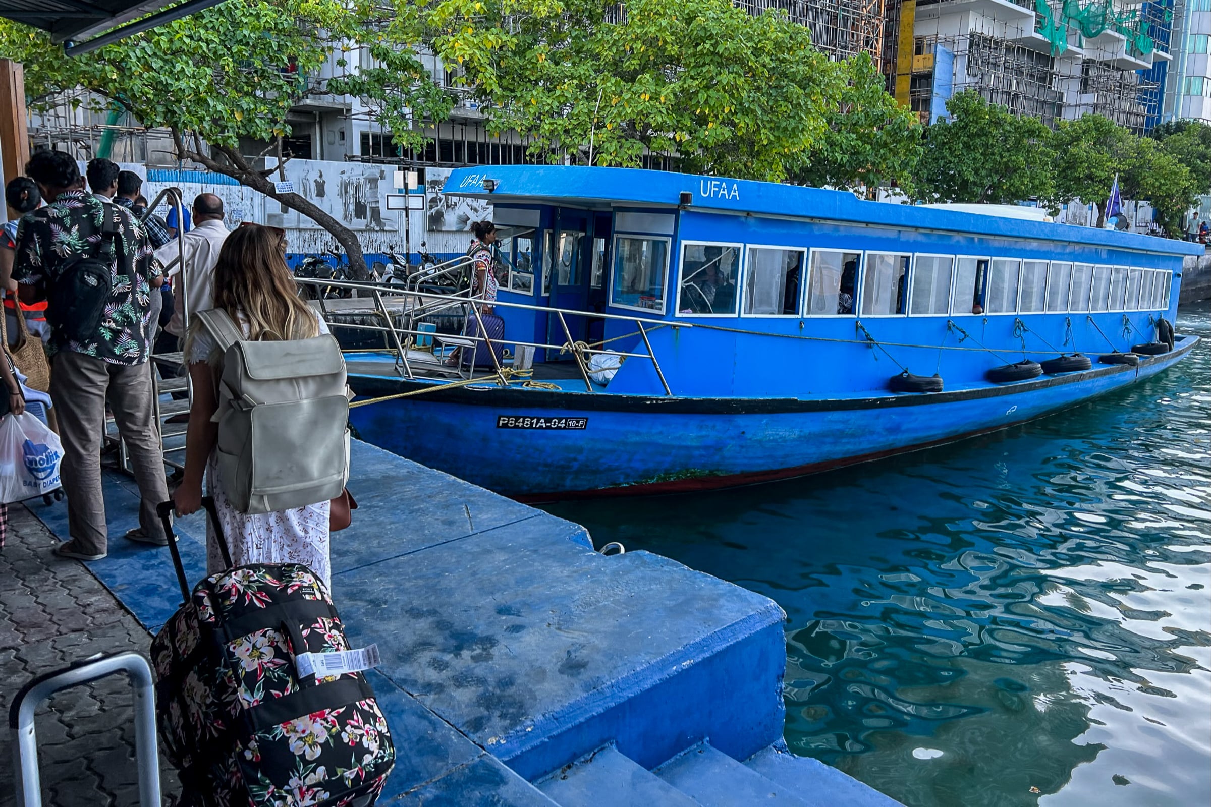 A queue of people waiting to board a blue ferry in the Maldives
