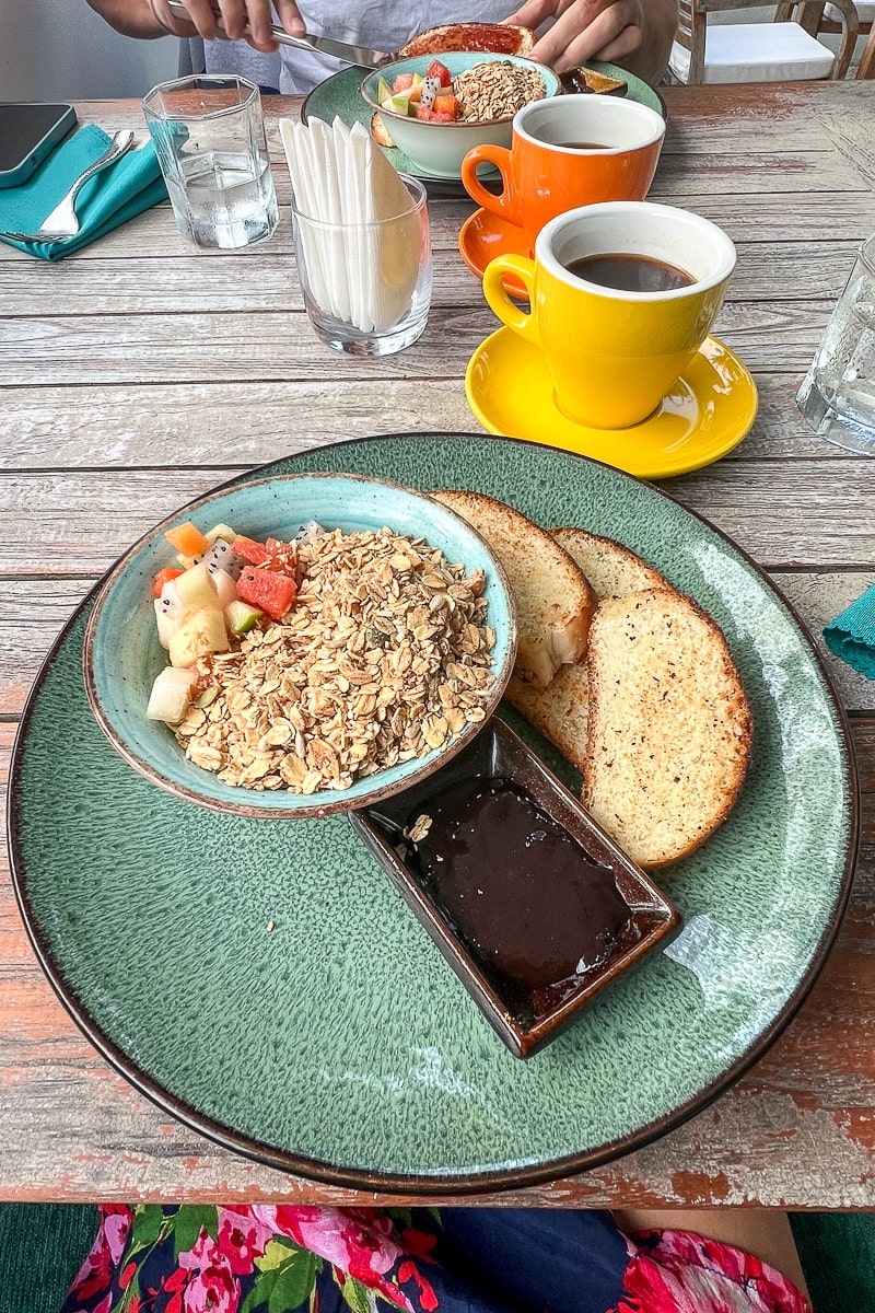 A breakfast plate with bowl of muesli, toast, coffee served on a rustic wooden table