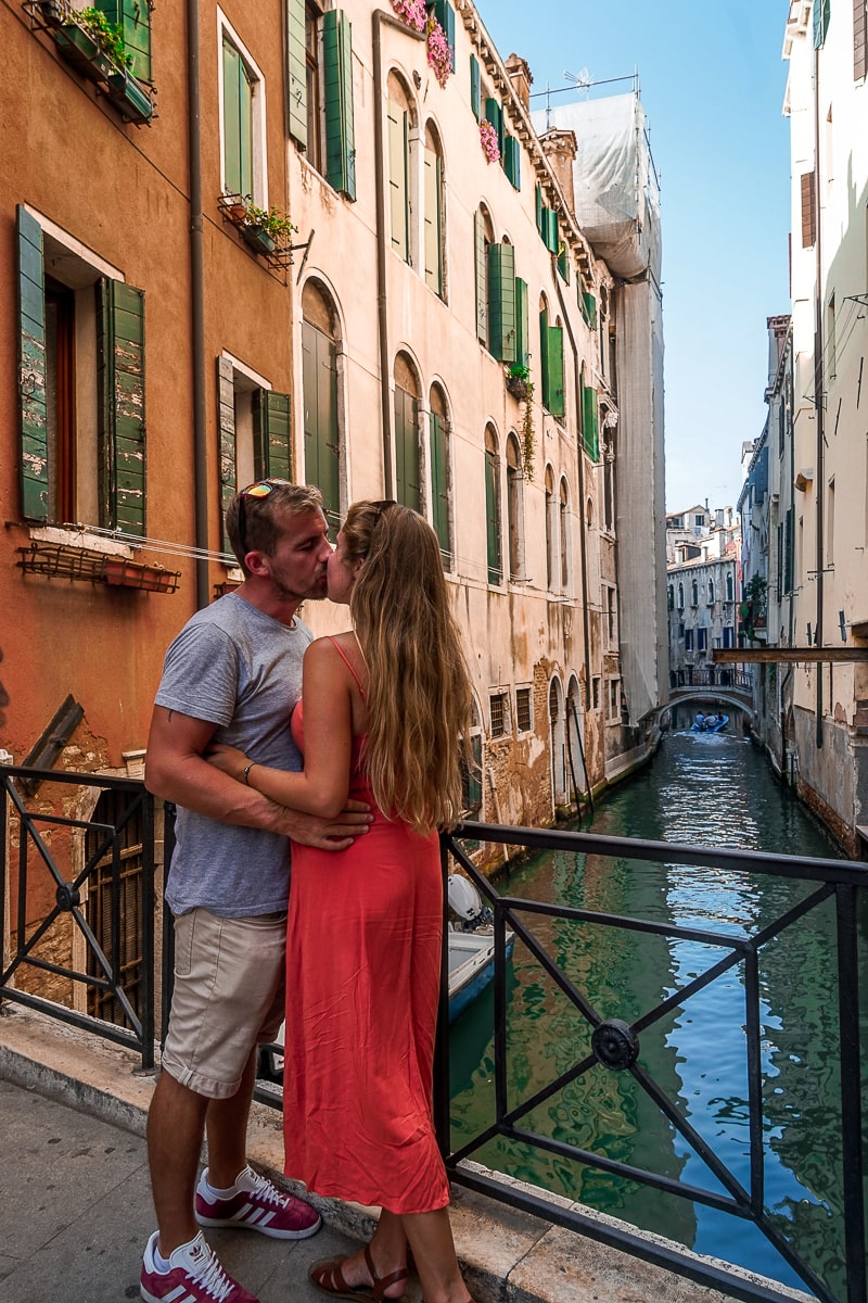 A couple kissing on a bridge in venice with colorful houses behind