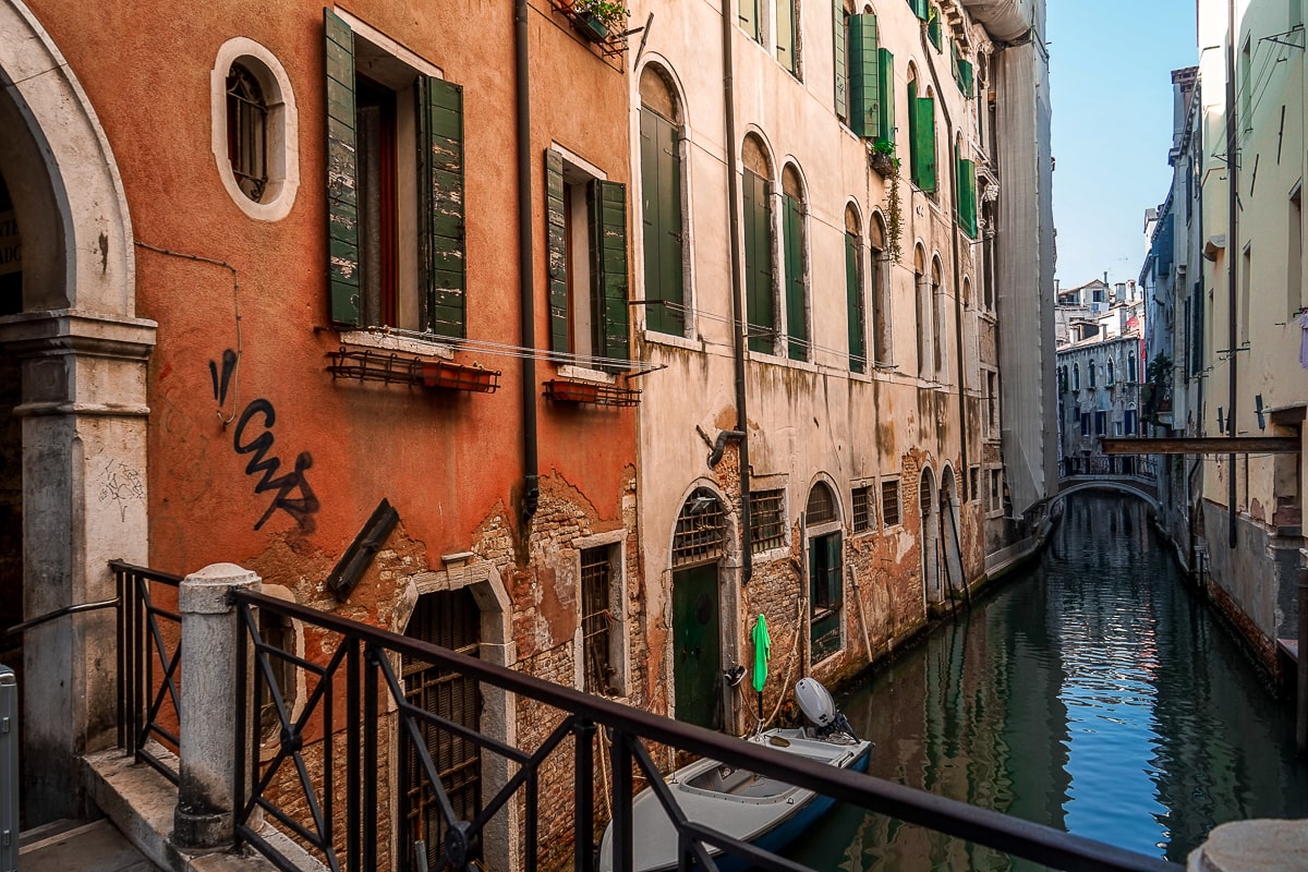 A venice canal view from a small iron bridge with pink and red houses and a small boat