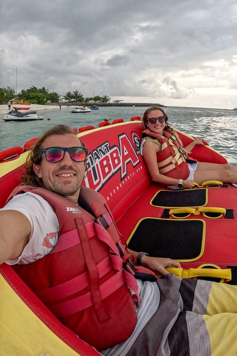 A selfie of a couple sat on a large inflatable sofa in the sea with a beach behind