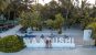 A drone shot of a couple sat on a large "Maafushi" white statue sign with sculptures of marine life