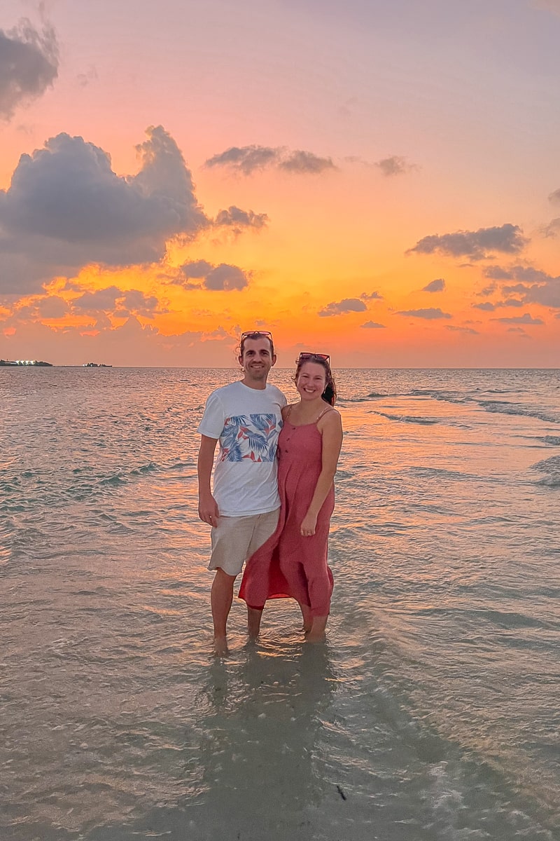 A couple stand arm in arm in the sea at sunset