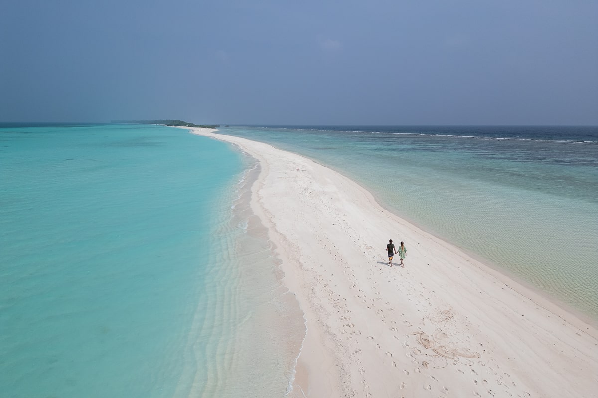 A couple running on a bright white sandbank with clear turquoise sea