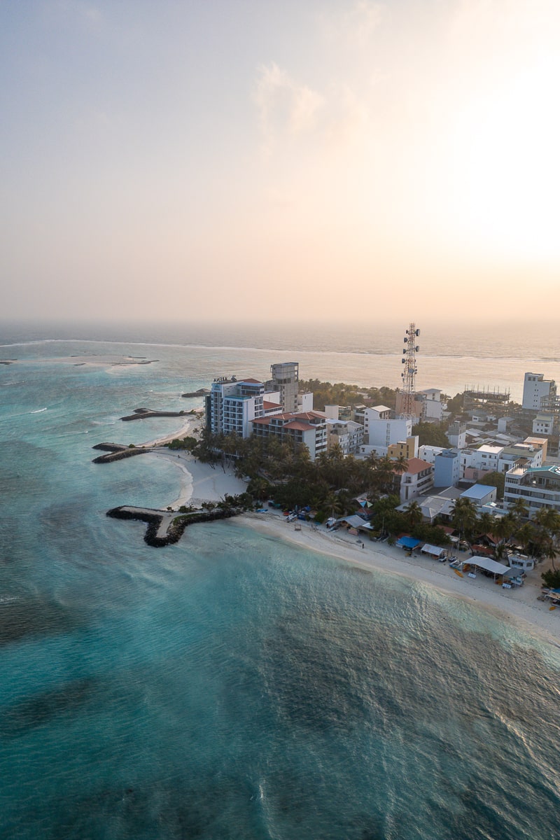 An aerial shot of the sunrise at the northern end of Maafushi - clear, blue waters, palm trees, and hotels