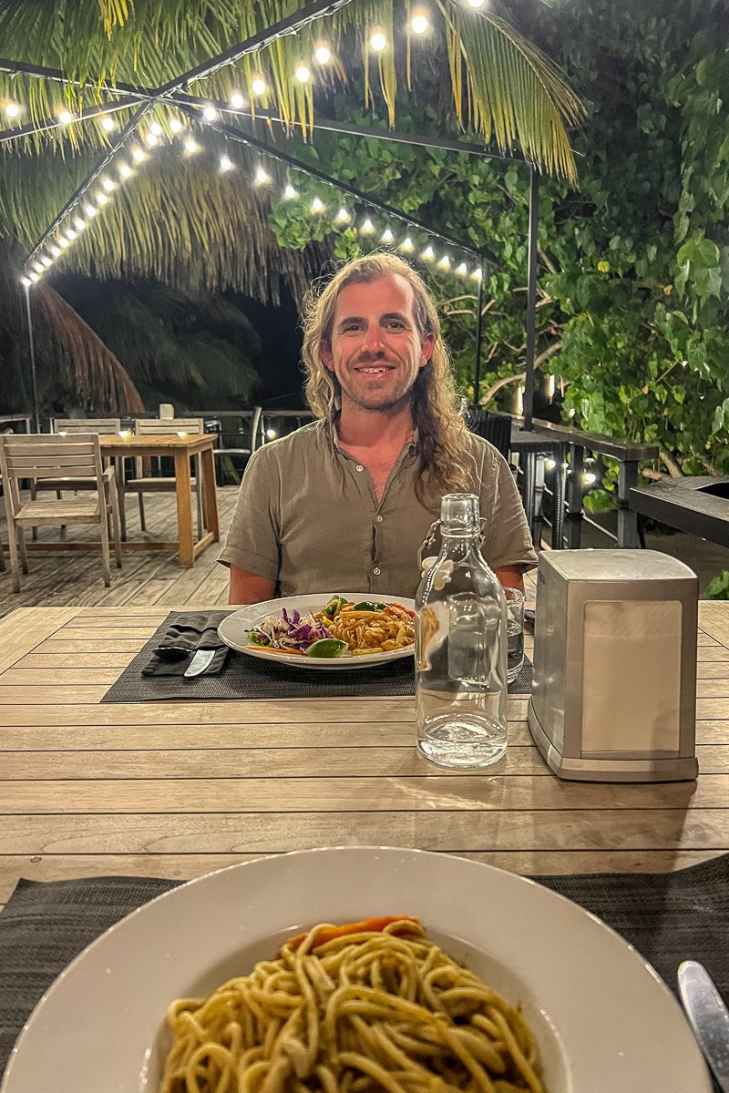 A point of view of a pasta dish and a man sat opposite with another pasta dish