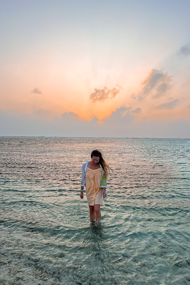A girl in a peachy dress walking out of the shallow sea around Maafushi at sunset