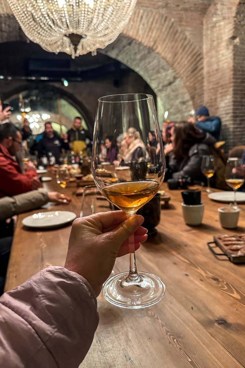 Holding a glass of amber wine in a wine cellar