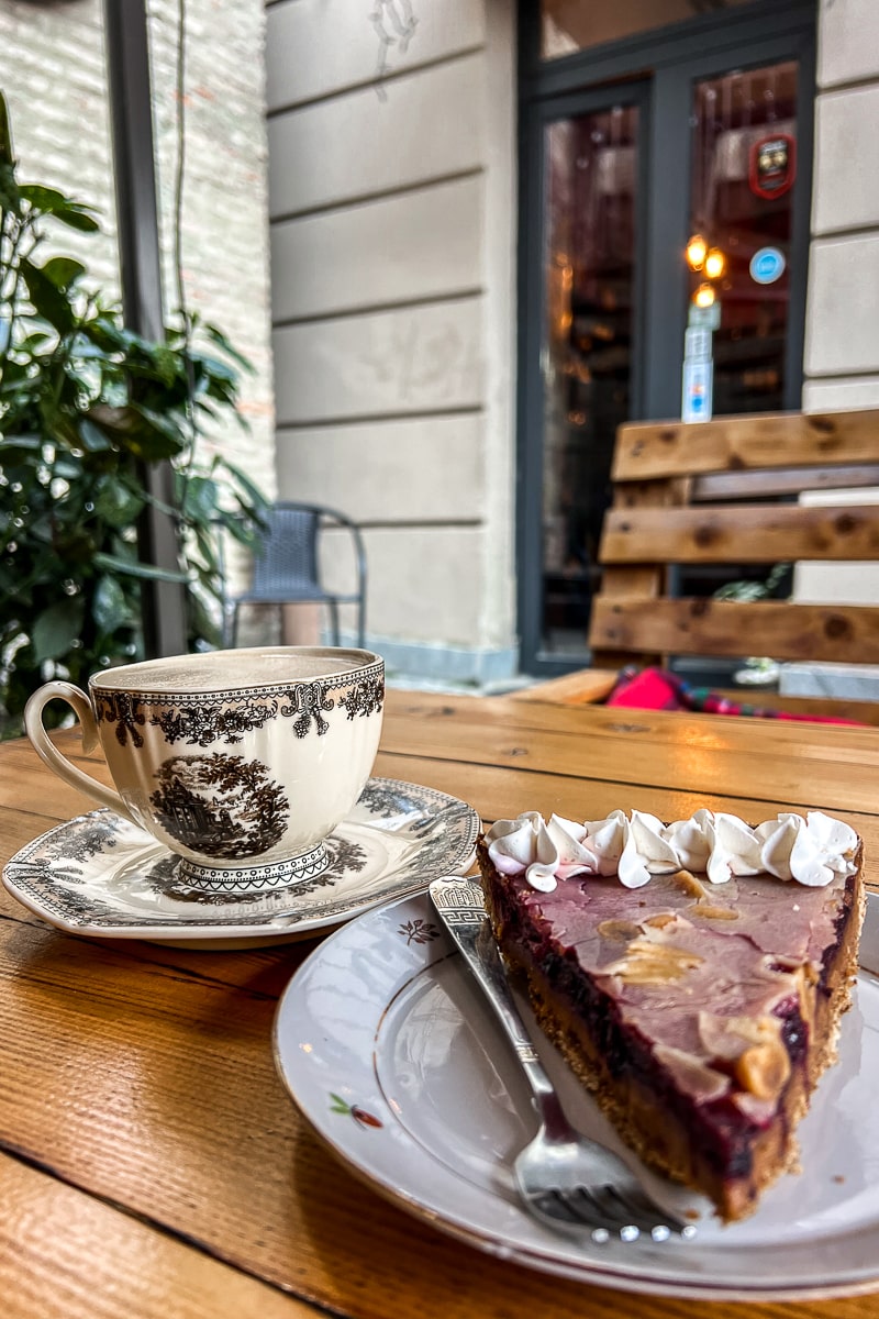 A slice of chocolate cake with cream and a coffee in an ornate china cup outside a cafe