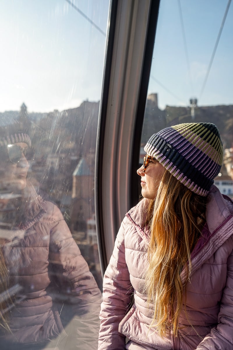 A portrait of a girl in a winter jacket and hat looking through the window of a cable car