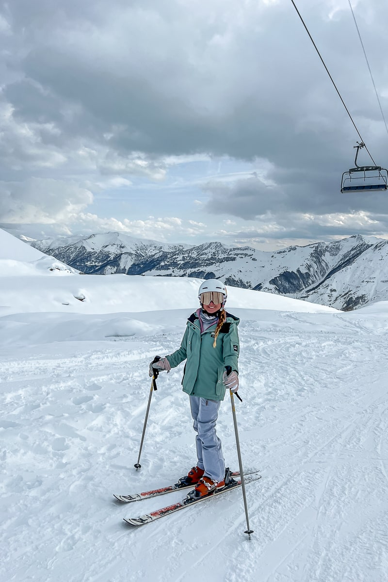A girl standing on skis on a ski slope as a chairlift passes overhead