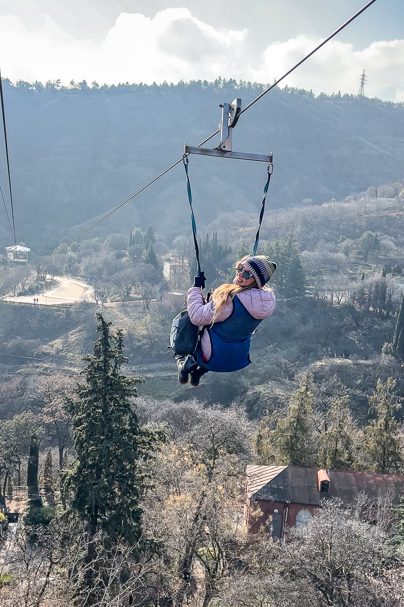 A girl smiling happily while ziplining over a botanic garden
