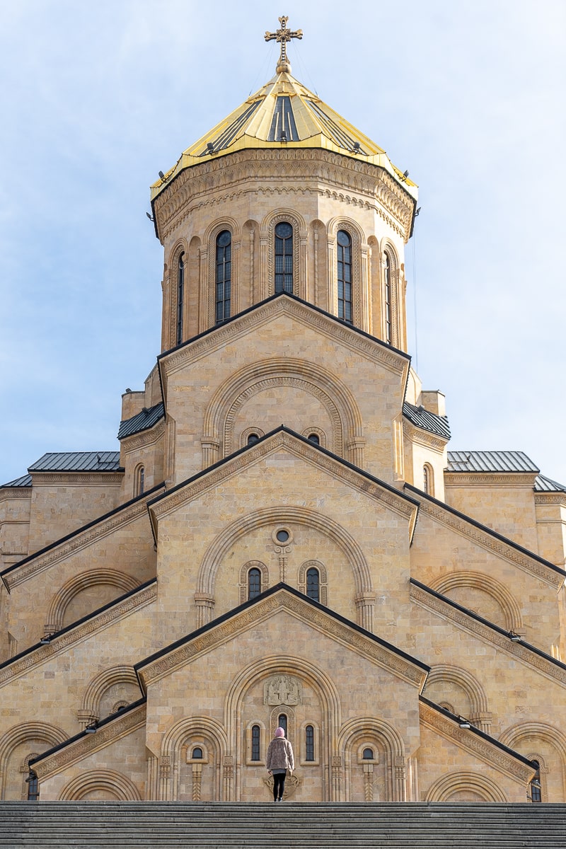A huge Eastern Orthodox cathedral with golden roof towering over a girl stood at the top of steps
