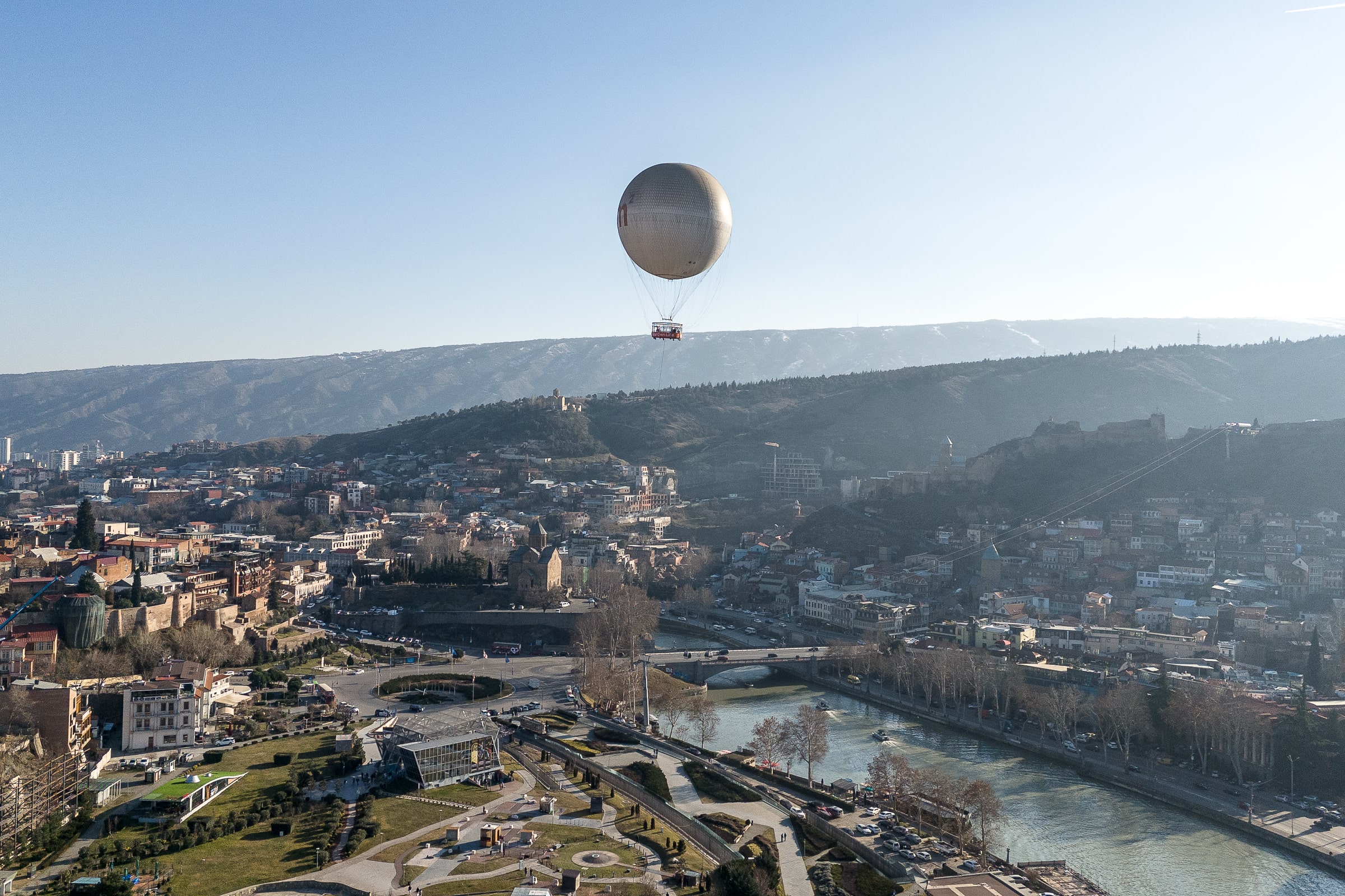 A panoramic shot of Tbilisi with the river featuring prominently and a hot air balloon in the sky
