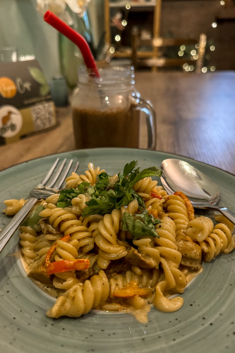 A vegan pasta dish in a sage green dish, a chocolate milkshake in the background