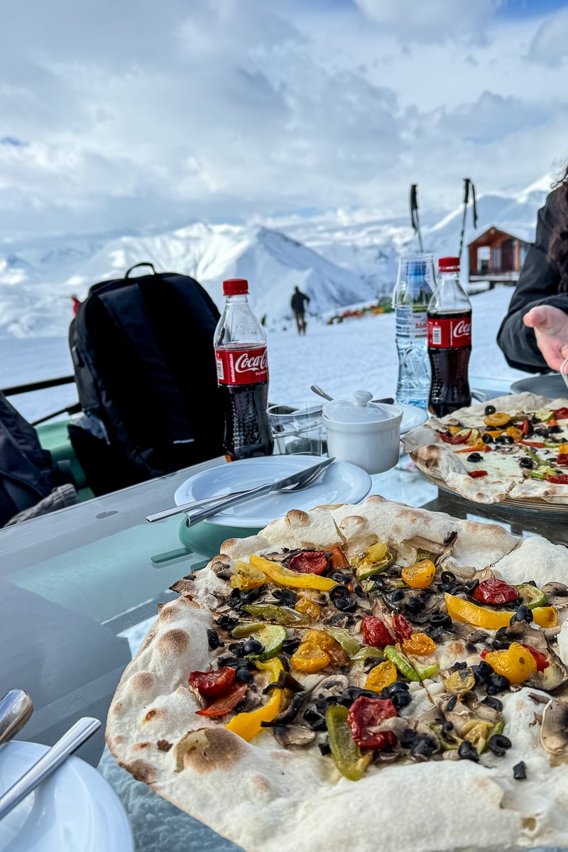 A vegetable pizza with a view of ski slopes in the background