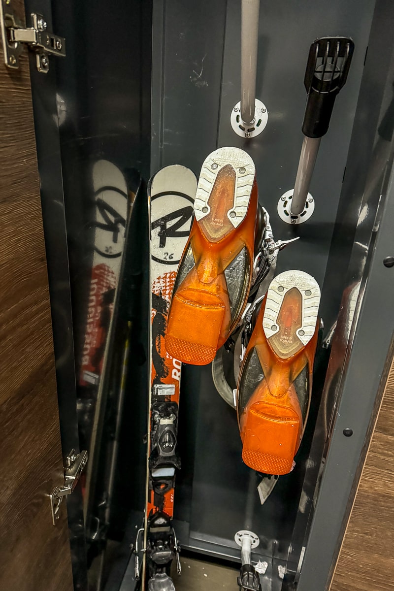 A set of orange ski boots and black, white, and red skis in a locker