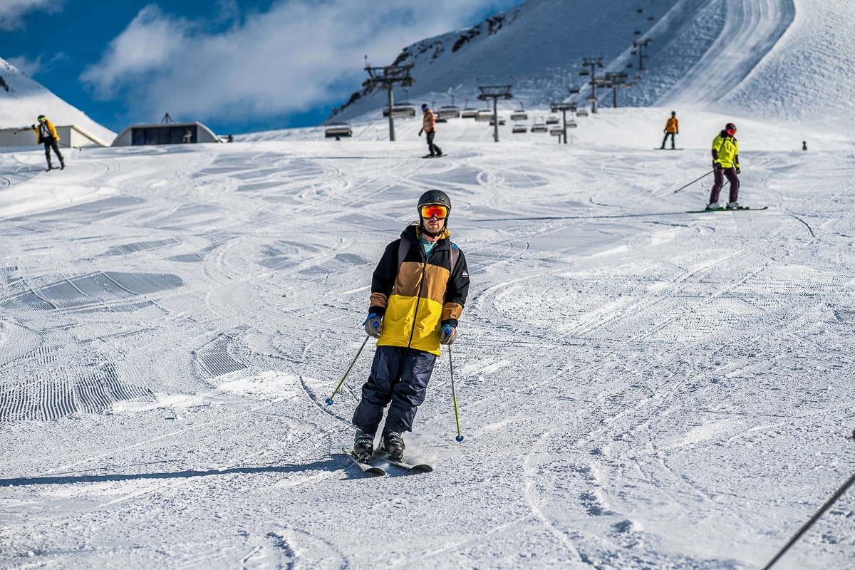 A man in a yellow and black jacket skiing down a slope with other skiers in the background