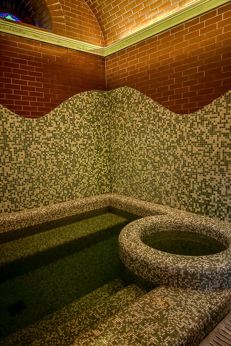 A hot tub and plunge pool inside a spa with blue and white tiles and red brick interior