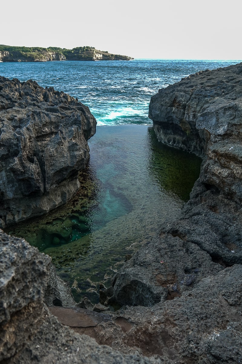 A billabong with calm, clear water and a blue ocean behind