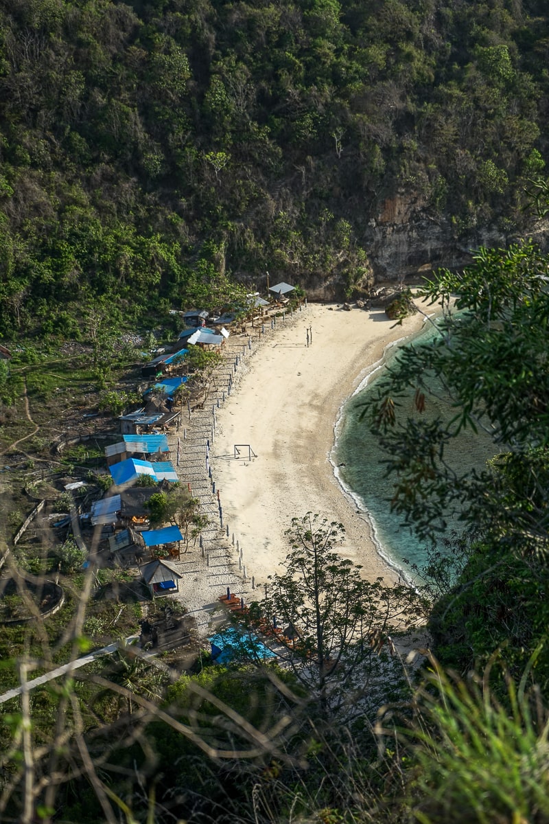 A sandy beach surrounded by lush vegetation. There are shacks along the back of the beach