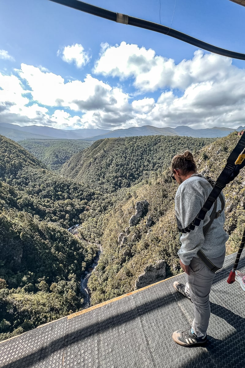 A man attached to a harness standing looking over the edge of a bridge