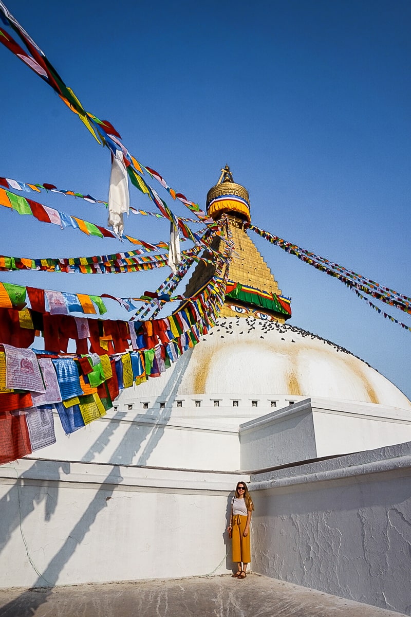 A woman standing on a white and gold stupa with prayer flags leading to the top of the structure