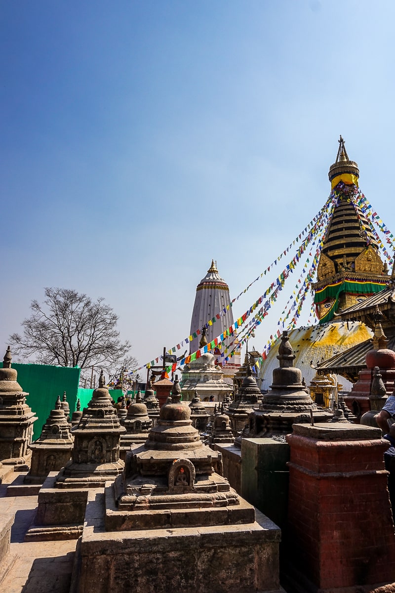 A set of Buddhist stone stupas and a large gold and white stupa with Buddha's eyes painted