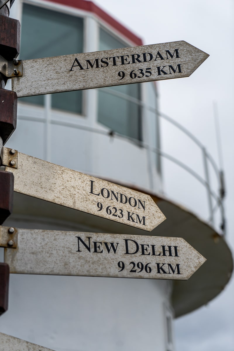 A lighthouse with distance signs for Amsterdam, London, and New Delhi