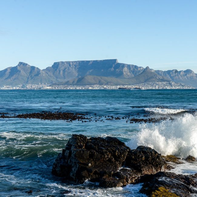 A wave crashing against a rock and Cape Town with the iconic Table Mountain in the background