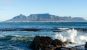 A wave crashing against a rock and Cape Town with the iconic Table Mountain in the background