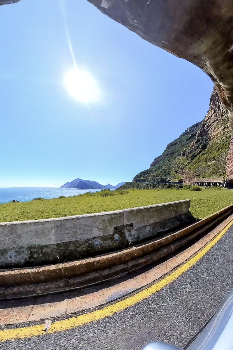 A rocky overhang on a road and a view of the ocean