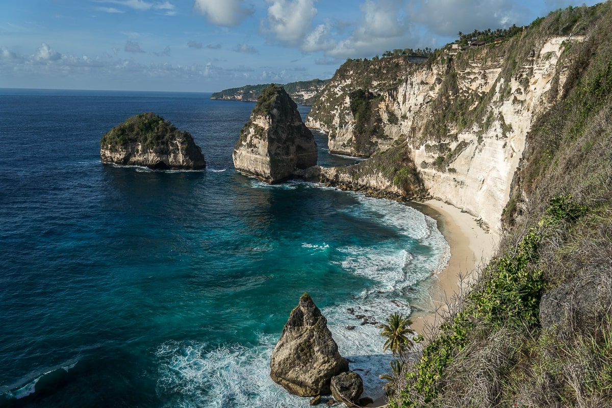 Beautiful blue ocean with white sandy beach and steep rocky cliffs