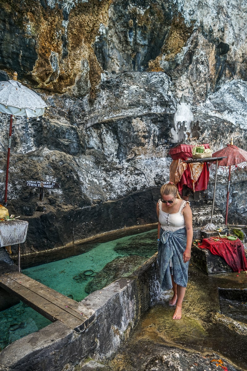 A woman bathing her feet at a water temple in cave-like setting