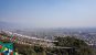 A panoramic view of Kathmandu, densely packed houses stretching to the horizon. Strings of prayer flags hang in the foreground