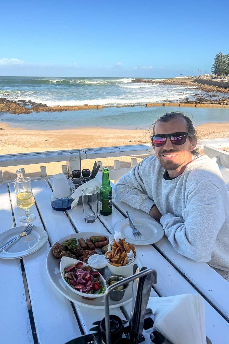 A man on a white bench with food at the beach