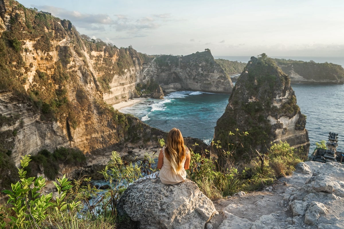 A woman sat on a rock overlooking the azure ocean with sharp pointed islands protruding from the sea